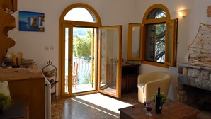 Ein Zimmer mit Kamin aus Stein, einem Esstisch mit Weingläsern und Blick durch eine Glastür auf einen Außenbereich mit einem Stuhl.
