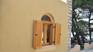 Ein Fenster mit Holzhörnern, eine Steinwand und ein Baum im Hintergrund.