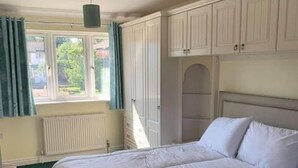 Quarto com uma cama de casal, janela com cortinas e radiador.