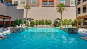 A swimming pool with a stone border, surrounded by lounge chairs and umbrellas.