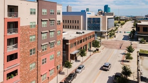 A multi-story building with a mix of brick and modern facades, a central courtyard, and a street view with cars and a clear sky.