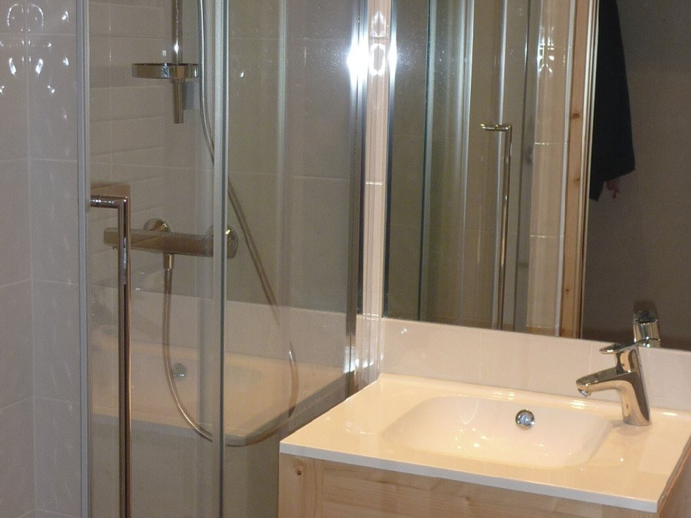 A modern bathroom with a glass-enclosed shower, a white sink, and a mirror.