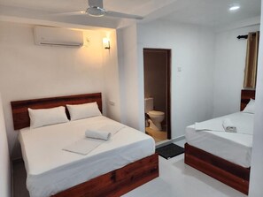 A hotel room with a large bed, a smaller bed, a wooden headboard, a ceiling fan, and a wall-mounted air conditioning unit. - Island Inn Colombo00 (Colombo)