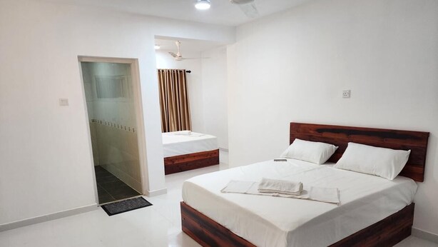 A bedroom with a wooden bed frame, white bedding, and a glass shower enclosure. - Island Inn Colombo00 (Colombo)