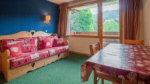 Una habitación acogedora con un sofá cama de madera, una mesa de comedor y un ventanal con vistas a zonas verdes y colinas.