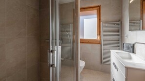 A modern bathroom with a glass shower enclosure, a toilet, and a vanity with a mirror. - Modern 2-Bedroom Apartment in Morzine Center with Parking and Wifi (Morzine)