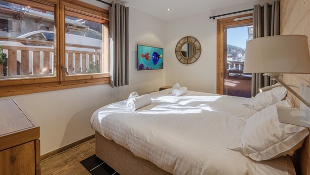 A hotel room with a bed, a painting, a mirror, and a view of the outside. - Modern 2-Bedroom Apartment in Morzine Center with Parking and Wifi (Morzine)