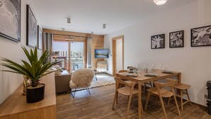 A dining area with a wooden table and chairs, a potted plant, and artwork on the walls. - Modern 2-Bedroom Apartment in Morzine Center with Parking and Wifi (Morzine)