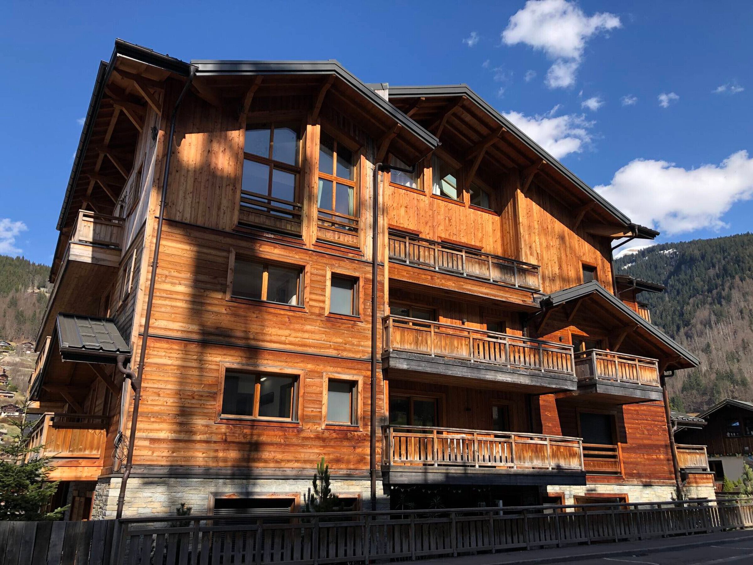 A multi-story wooden chalet with balconies, large windows, and a mountainous backdrop.