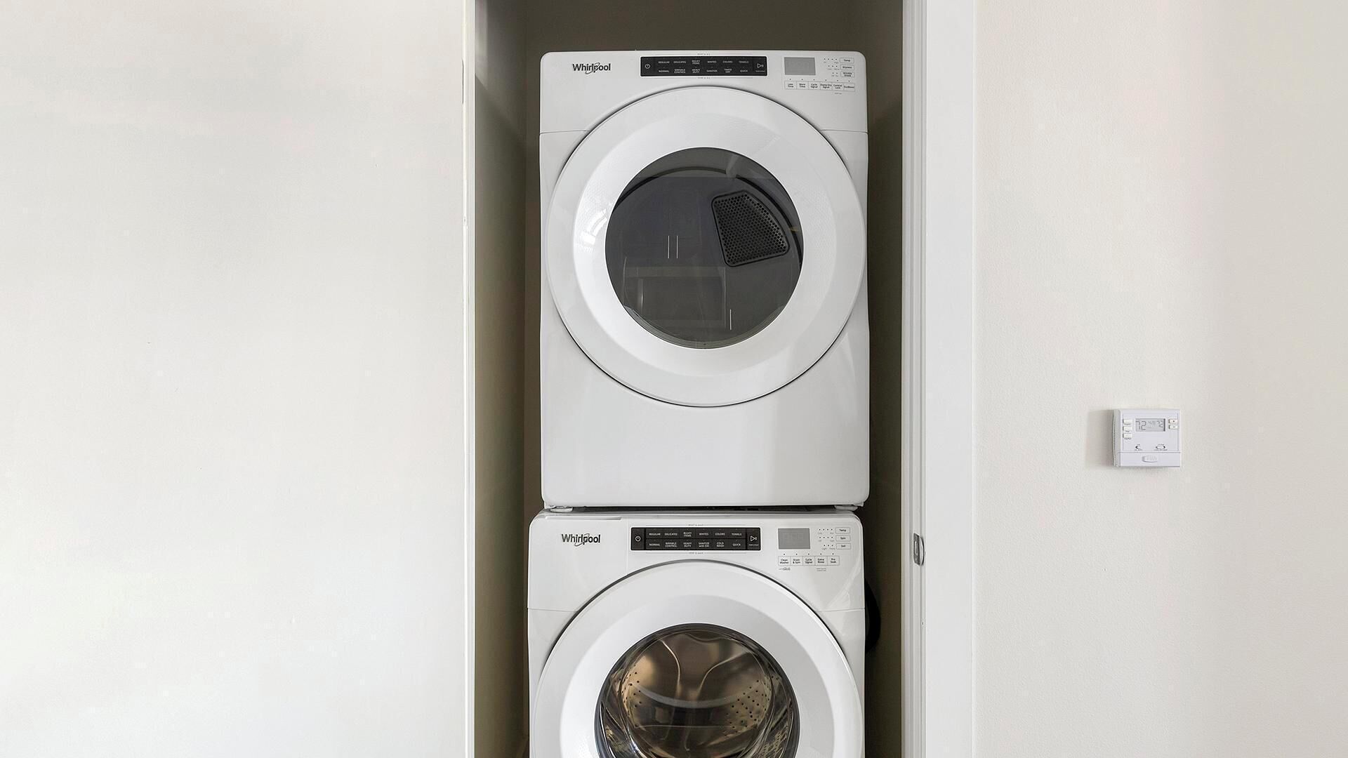 A stacked washer and dryer unit with control panels and a power outlet on the wall.