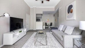 A modern living room with a flat-screen TV, a sofa, a coffee table, and a dining area with a table and chairs. - Landing | Stunning 1BD, Pool, Gym (Houston)