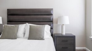 A bedroom with a dark headboard, a white bedspread, and two bedside tables with lamps and drawers. - Landing | Stunning 1BD, Pool, Gym (Houston)
