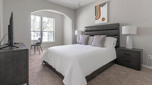 A modern bedroom with a large bed, bedside lamps, a TV on a stand, and a window with blinds. - Landing | Stunning 1BD, Pool, Gym (Houston)