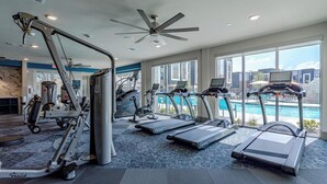 Une salle de sport équipée de tapis de course, de vélos d’appartement et d’appareils de musculation, avec de grandes fenêtres et un ventilateur de plafond.
