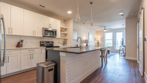 A modern kitchen with white cabinets, a stainless steel refrigerator, a microwave, and a large island with bar stools.