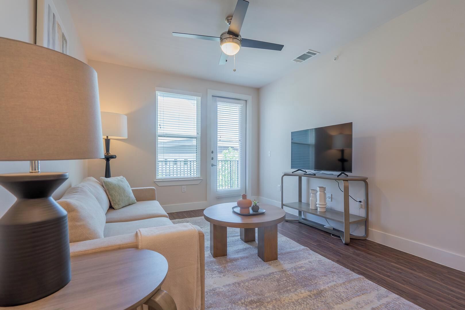 Un salon comprenant un canapé, une table basse, une lampe, un téléviseur posé sur un meuble et un ventilateur de plafond.