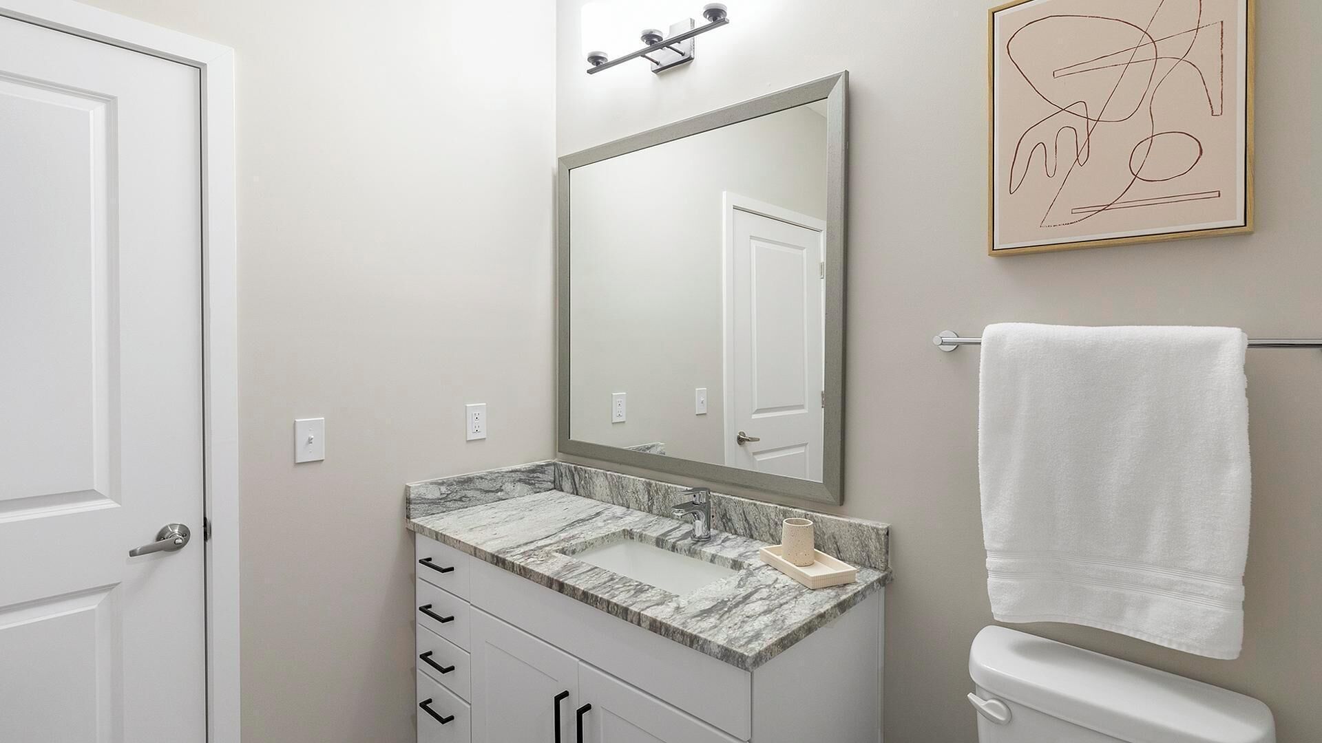 A bathroom with a marble sink, a large mirror, a towel rack, and a framed artwork on the wall.