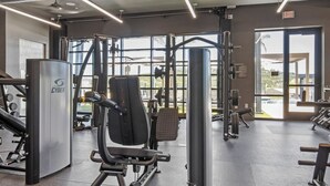 Ett gym med olika typer av träningsredskap, stora fönster och en utrymningsskylt.