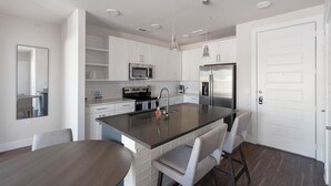 A modern kitchen with white cabinets, stainless steel appliances, and a central island with bar stools. - Landing | Chic 2BD, Gym, Clubhouse (San Antonio)
