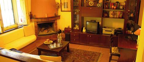 Un salon avec une cheminée, un canapé, une table basse et une bibliothèque remplie de livres et d’objets décoratifs.