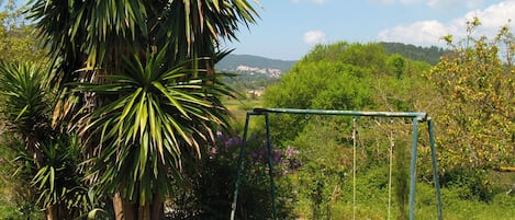 Une balançoire installée dans un espace verdoyant, avec un grand arbre et une vue sur des collines lointaines.