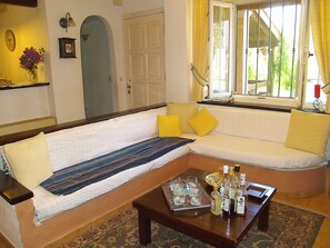 Uma sala de estar com sofá, uma mesa de centro com garrafas, um relógio e uma janela com cortinas.