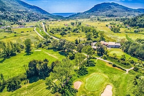 An aerial view of a rural landscape with a golf course, scattered houses, and a mountain range in the background. - Holiday House Near the Beach of Ermones and Mirtiotissa in Vatos Corfu (Corfu)