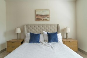 A bed with a tufted headboard, two bedside tables with lamps, and a painting on the wall.