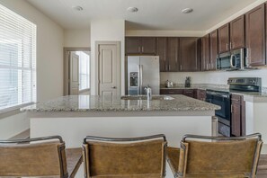 A kitchen with granite countertops, dark wooden cabinets, stainless steel appliances, and a central island with bar stools.