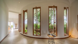 A spacious hallway with large windows, a round wooden table, and a lamp.
