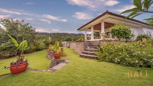 A house with a covered porch, a stone wall, and a grassy garden with potted plants.
