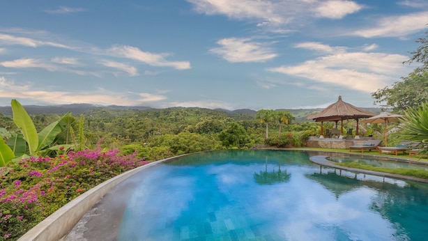 A pool with a gazebo and lounge chairs, surrounded by lush greenery and mountains in the background.