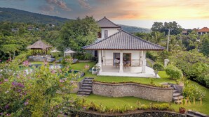 A villa with a tiled roof, a pool, and lush gardens.