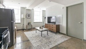 A modern kitchen with a refrigerator, stove, and microwave. There is a dining area with a table and chairs. A television is mounted on the wall, and a cabinet is visible. - Landing | Modern 1BD, Gym (Birmingham)