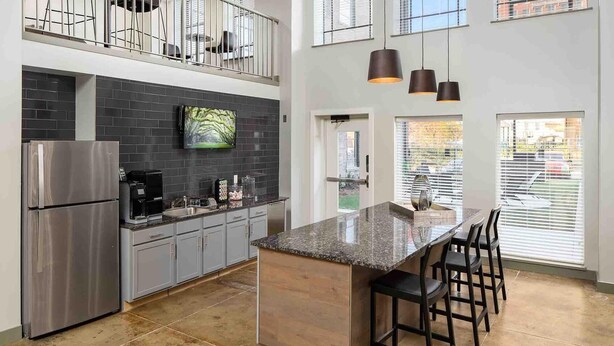 Eine moderne Küche mit Edelstahl-Kühlschrank, grauen Schränken, einer Kücheninsel mit Granitplatte und Barhocker sowie Pendelleuchten.