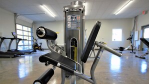 Ein Fitnessstudio mit unterschiedlichen Trainingsgeräten, darunter eine Beinpresse, Laufbänder und Ergometer.