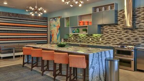 A modern kitchen with a central island, bar stools, a painting, and built-in appliances. - Landing | Spectacular 1BD, Gym, Pool (Spring)
