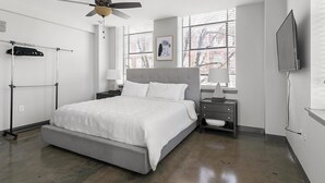 Ein Schlafzimmer mit Bett, Nachttischen, Deckenventilator, Fenster mit Jalousien und Fernseher an der Wand.