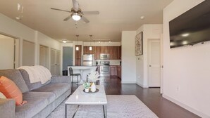 A modern living room with a gray sofa, a coffee table, and a kitchen in the background. - Landing | Beautiful 2BD, Yoga Studio, Clubhouse (San Antonio)