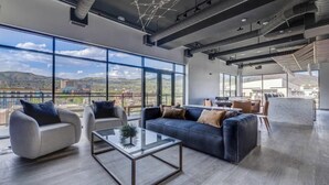 A spacious living area with a large window, a sofa, a coffee table, and a dining area with chairs. - Landing | Modern 1BD, Courtyard, Clubhouse (Salt Lake City)