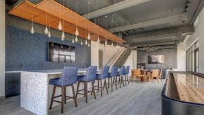 A modern bar area with a long counter, blue upholstered bar stools, and pendant lighting. - Landing | Incredible 1BD, Yoga Studio, Gym (Salt Lake City)