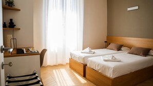 A hotel room with two beds, a desk with a chair, a mirror, and a window with sheer curtains. - Testaccio Design Apartment in Rome - to feel the authentic vibe! (Roma)