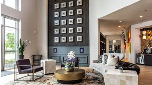 A modern living room with a large wall of framed pictures, a round coffee table with a floral centerpiece, and a sofa with decorative pillows. - Landing | Incredible 1BD, Courtyard, Gym (Fort Worth)