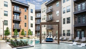 A modern apartment complex with a swimming pool, lounge chairs, and a covered seating area. - Landing | Incredible 1BD, Courtyard, Gym (Fort Worth)