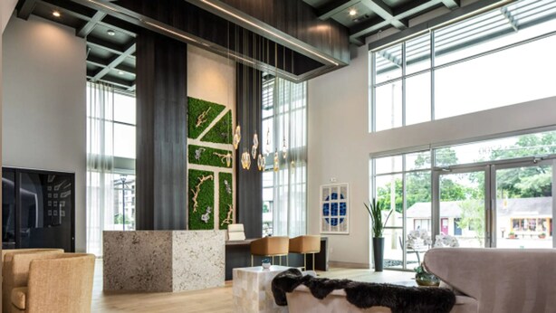 A spacious lobby with a high ceiling, large windows, a central green wall with art, and a seating area with chairs and a sofa. - Landing | Incredible 1BD, Courtyard, Gym (Fort Worth)