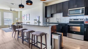 A modern kitchen with dark cabinets, stainless steel appliances, and a bar area with stools. - Landing | Incredible 1BD, Courtyard, Gym (Fort Worth)
