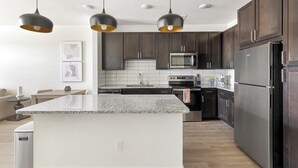 Une cuisine moderne avec des meubles de couleur sombre en bois, un réfrigérateur en acier inoxydable, un four à micro-ondes et un îlot central doté d’un comptoir en granit.