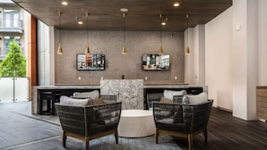 Une cuisine moderne avec un îlot en marbre, deux chaises en osier, des luminaires suspendus et une grande fenêtre donnant sur un paysage urbain.