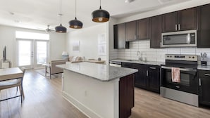 Une cuisine moderne avec des meubles de couleur sombre, un plan de travail en granit, des appareils électroménagers en acier inoxydable et des luminaires suspendus.