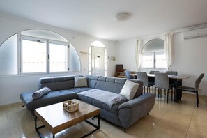 A modern living room with a sectional sofa, a coffee table, and a dining area with chairs and a table.